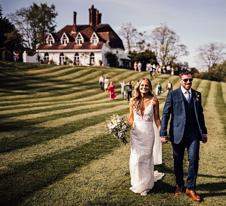 Bride and groom wearing sunglasses walk over to their reception 