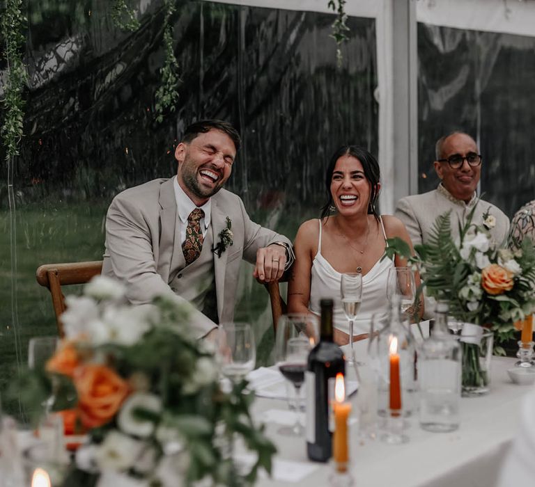 Bride and groom laughing during the clear marquee wedding reception speeches 