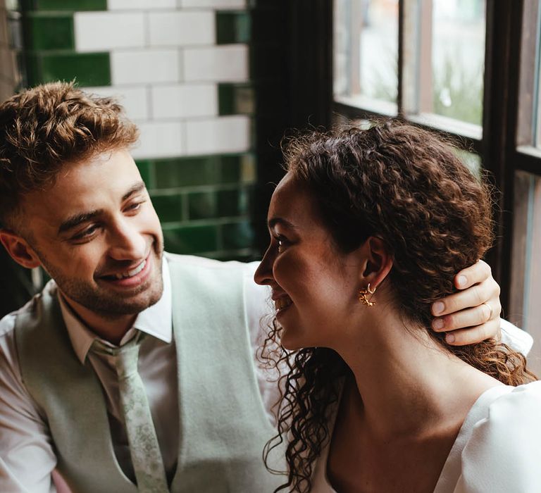 Groom in a pale green suit and tie holding his brides naturally hair back revealing her ear curation