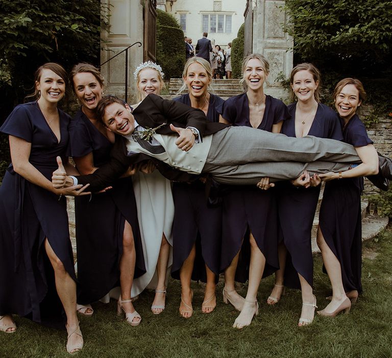 Bridesmaids in navy blue dresses and bride lift the groom together 