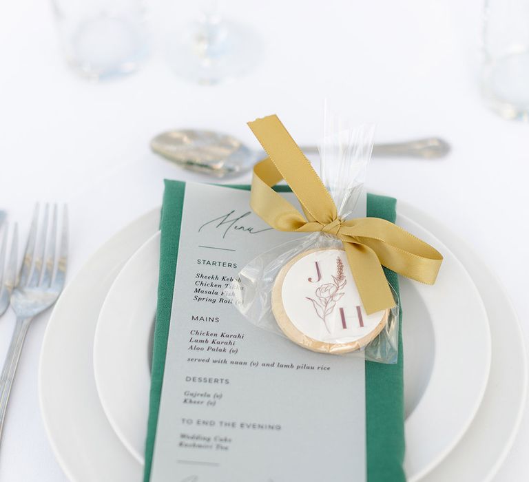 Green napkin sits on white plate complete with gold ribbon and personalised biscuit favours 