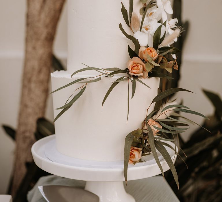 Two tier traditional white wedding cake with orange and green flowers and foliage 