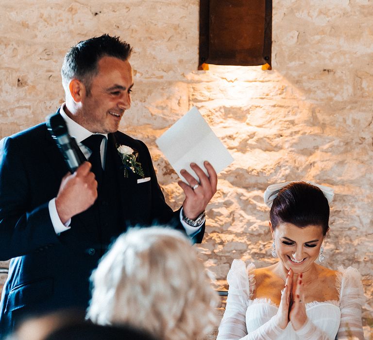 Bride with red hair and white hair bow claps as the groom reads out his speech 