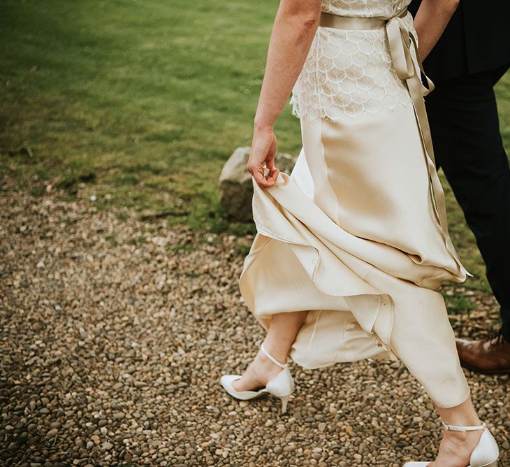 Bride who wears white ankle strap shoes with kitten heel walks with her groom 