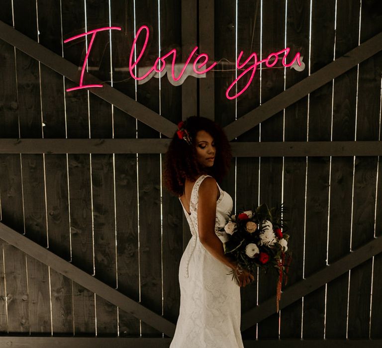 Bride in lace wedding dress stand under pink neon 'I Love You' sign