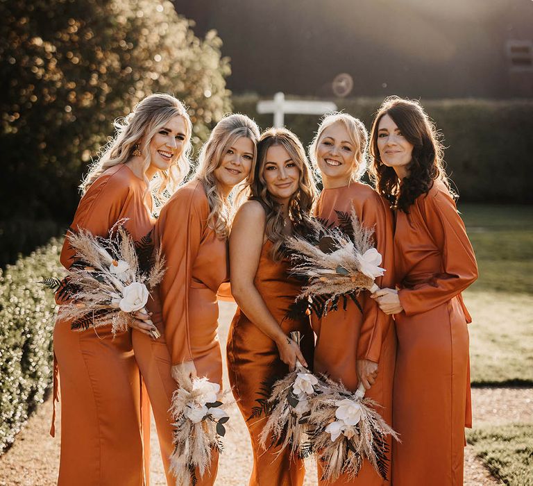 Bridesmaids in burnt orange dresses holding pampas grass bouquets with white flowers