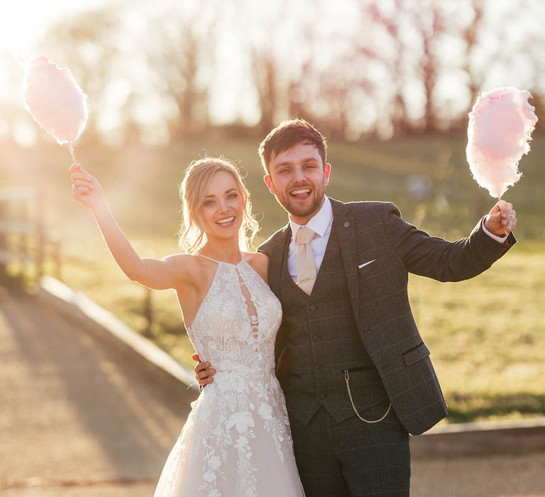 Bride in halter neck tulle wedding dress with groom in blue suit lifting their candy floss into the air 