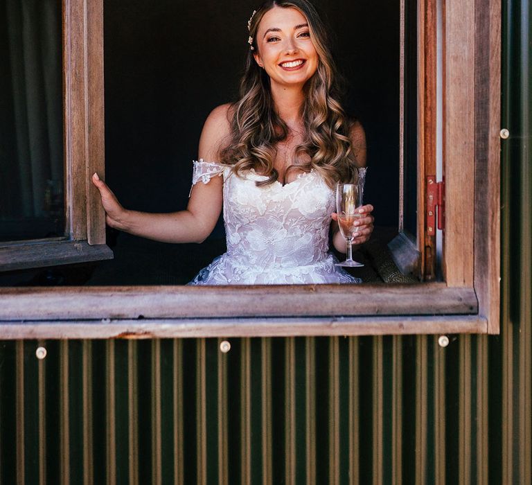 Bride in lace off the shoulder wedding dress smiling holding a glass of champagne 