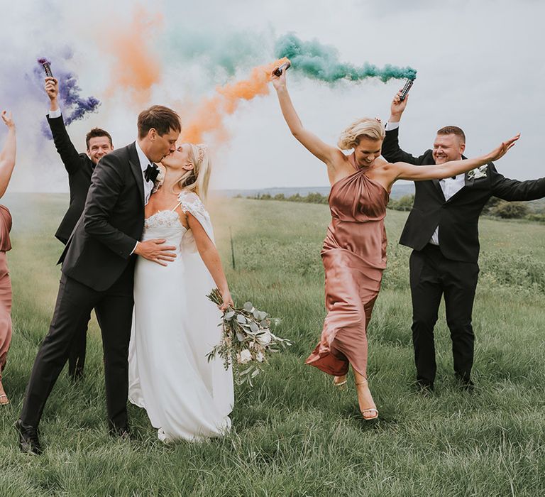 Bride and groom kiss as the bridesmaids and groomsmen wave colourful smoke bombs 