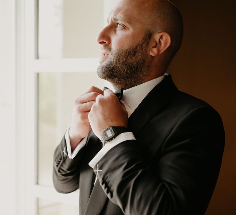 Groom adjusts his black bow tie on his wedding day in France