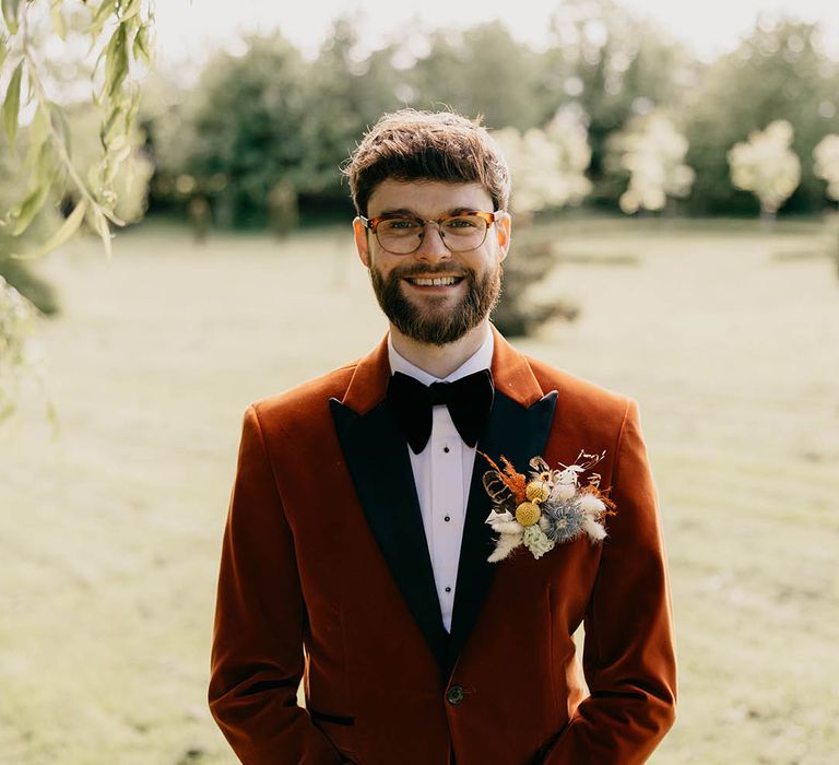 Groom in an orange tuxedo with a dried flower buttonhole 