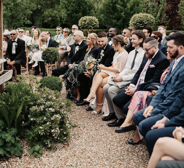 Wedding guests sit watching the outdoor wedding ceremony 