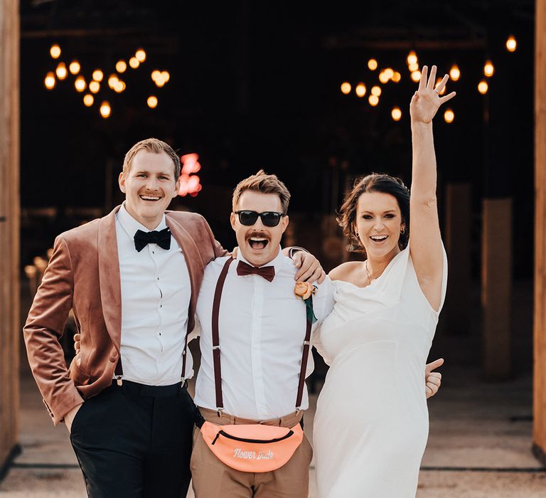 Groom in pink velvet suit jacket, bride in ASOS wedding dress, and flower dude with personalised bum bag for confetti