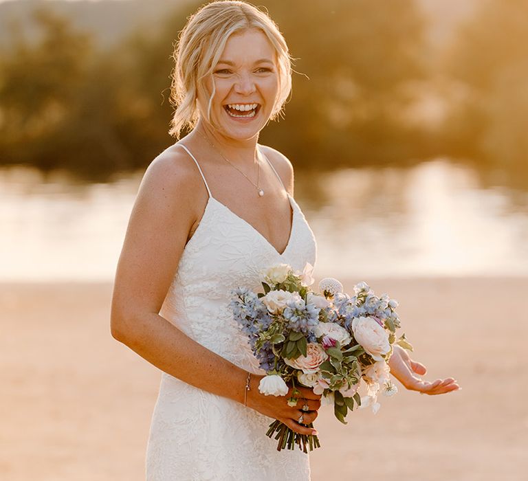 Blonde bride holds pastel floral bouquet and wears lace fitted wedding dress