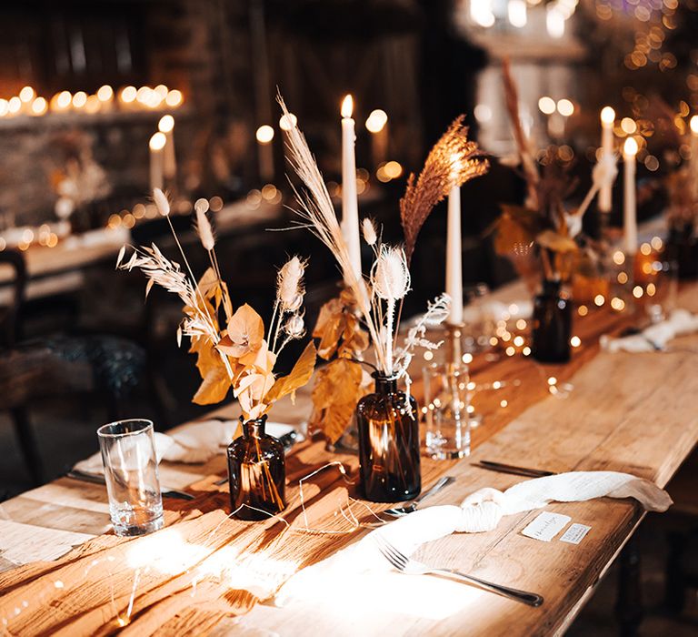 Small dried floral arrangements across wooden tables with orange fabric table runner 