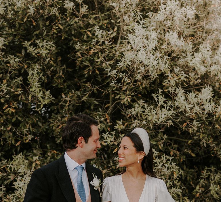 Groom in a morning suit with pink waistcoat and blue tie with the bride in a Ghost satin button wedding dress and pearl headband 