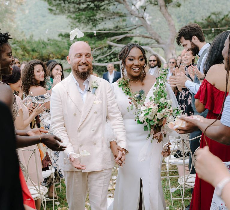 Bride and Groom walk through cream and peach coloured petal confetti whilst holding hands. The Brides something blue wedding shoes peep through her dress split