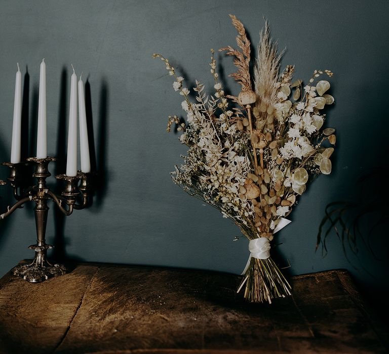 Rustic beige and white dried bouquet leans against dark wall