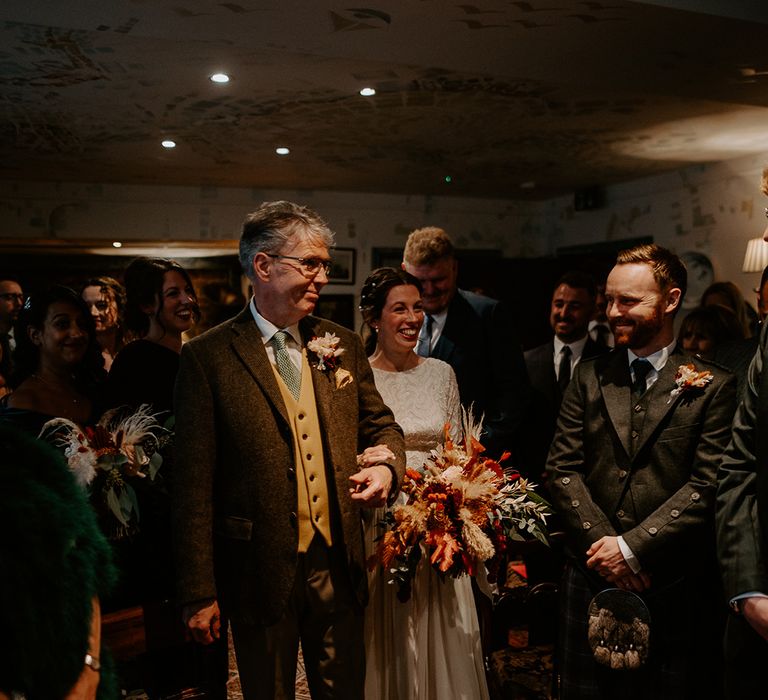 Bride in vintage lace wedding dress holding large autumnal bouquet with roses and pampas grass walking into wedding reception at The Zetter Townhouse