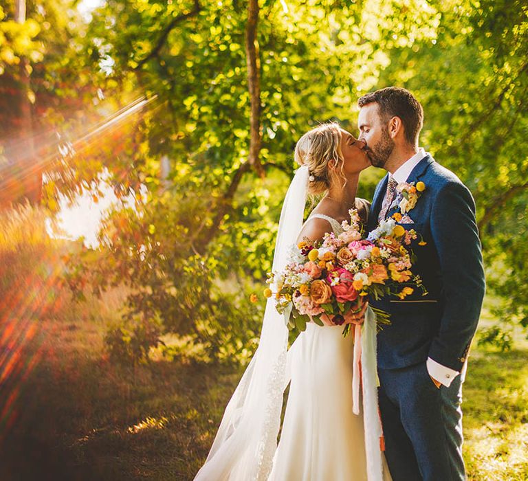 Bride and Groom kiss while Bride holds a colourful bridal bouquet in outdoor wedding photography