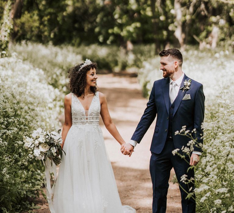 Bride in boho styled lace wedding dress holds hands with her groom outdoors 