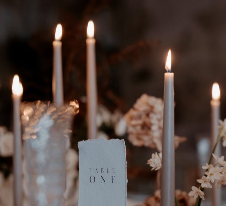 Minimalistic wedding white table number and beige tapered candles in clear candlestick holders 