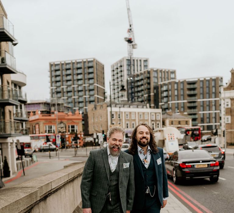 Grooms walk alongside one another in tartan suit and blue suit complete with matching floral tie and shirt and brogues 