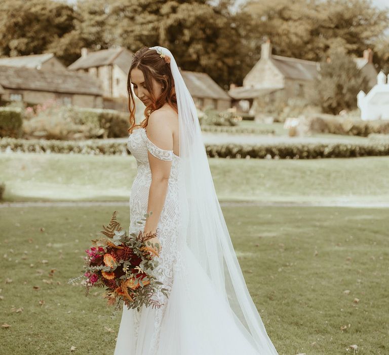 Bride in fitted off the shoulder boho lace wedding dress with embroidered veil for Disney theme wedding 