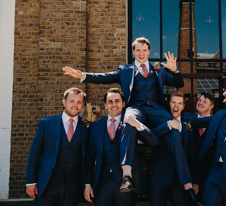 Groom is lifted by his groomsmen in three piece blue suits 