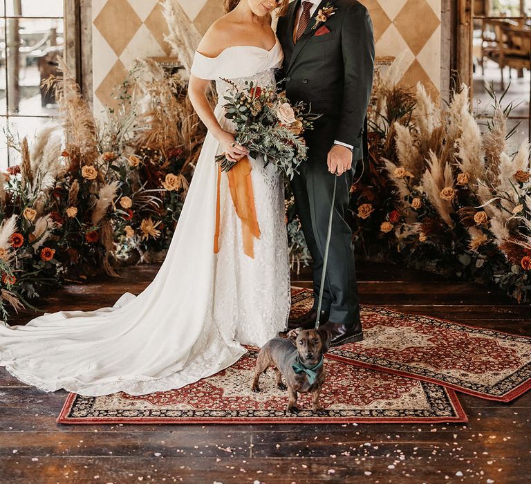 Bride in Love Spell wedding dress holds Autumnal wedding bouquet tied with orange raw edge ribbon