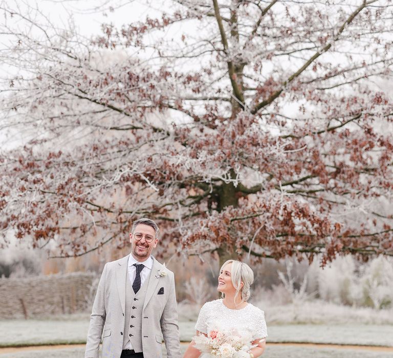 Groom in light grey suit jacket walking with the bride in a beaded short sleeve top and tulle bridal skirt