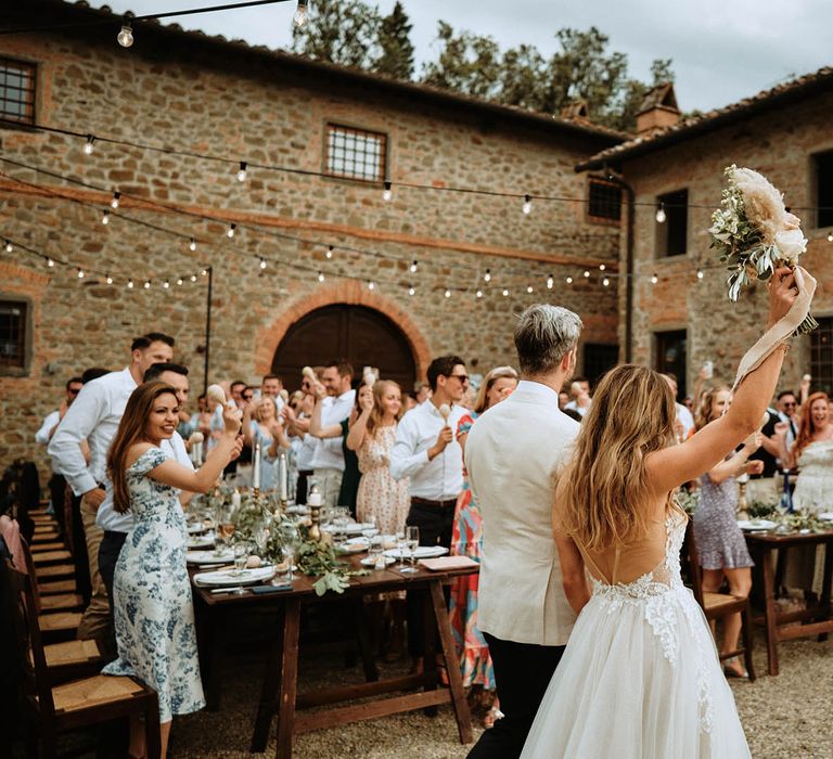 Couple wedding reception entrance showing brides backless wedding dress, pampas grass and eucalyptus bridal bouquet and Italian villa at destination wedding