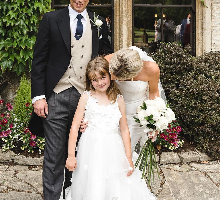 Flower girl in floral tulle dress with the bride and groom on their wedding day 