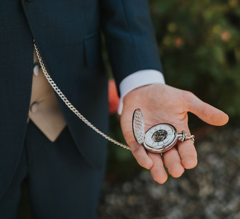 Groom in navy suit holding silver pocket watch groom accessory 