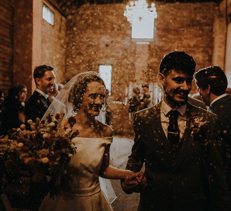 The bride and groom exit from the ceremony as their guests throw confetti over them 