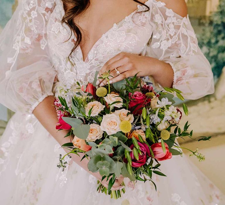 Bride in v-neck long sleeve shoulder cut out 3d appliqué wedding dress with flecks of gold holding large dried flower, eucalyptus, spring florals and garden rose bridal bouquet 