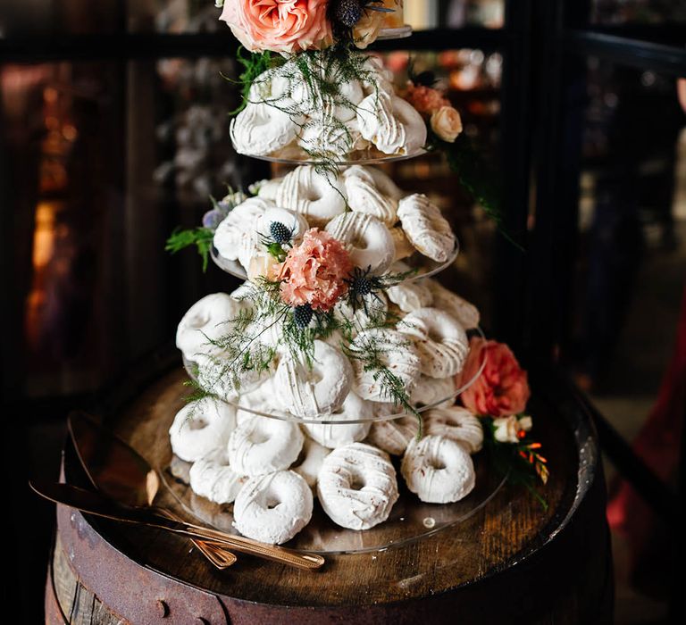 Doughnut tower made of white doughnuts with white iced wedding cake layer decorated with pink flowers 