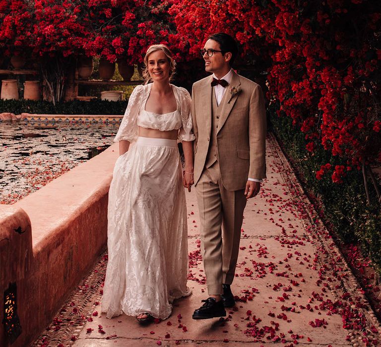 Bride and groom walking amongst red flowers in Marrakech for destination wedding 