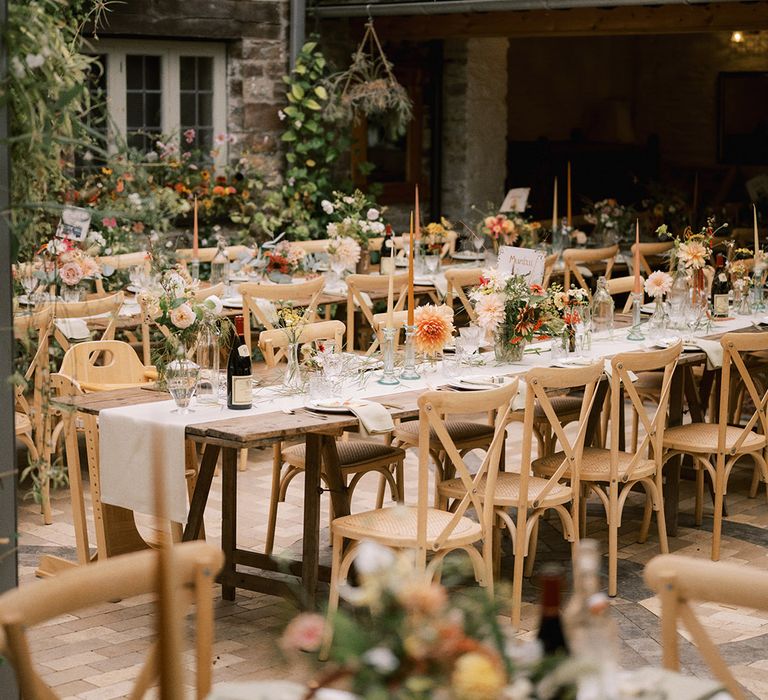 Beautiful wedding breakfast set up at Coombe Trenchard with cafe au lait dahlias, orange taper candles and unique table name signs