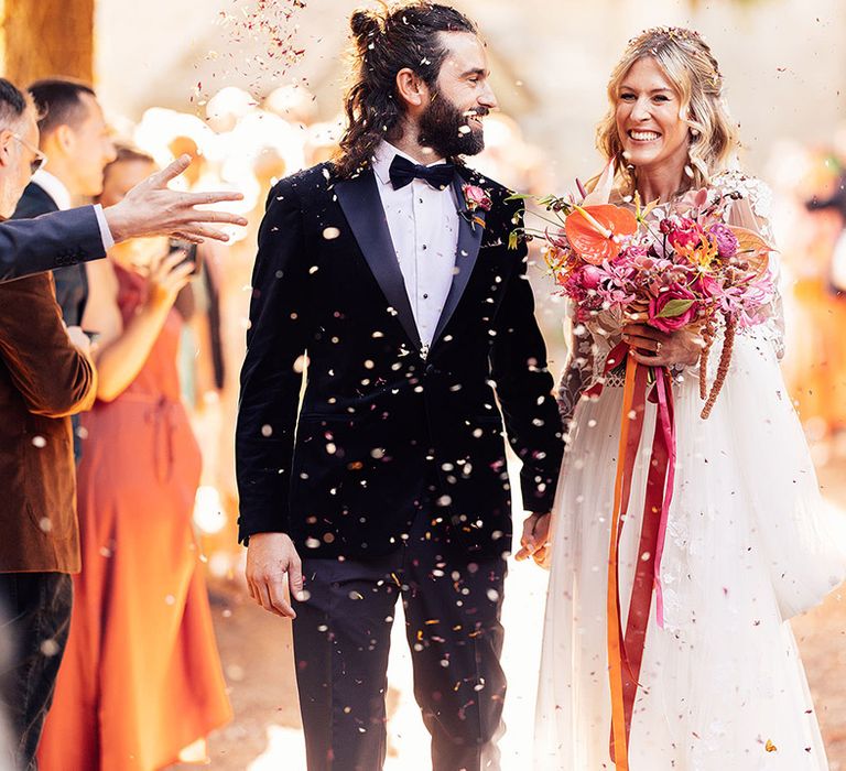 Bride holding a bright and colourful wedding bouquet with anthuriums and tropical flowers walking back down the aisle with the groom 