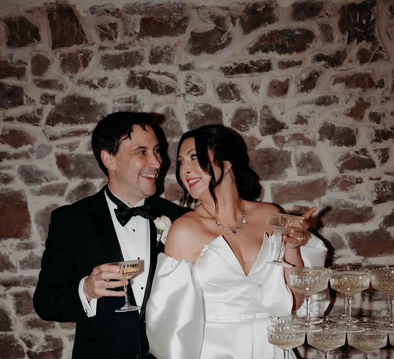 Bride and groom holding champagne coupes nect to a champagne tower at Upton Barn wedding venue