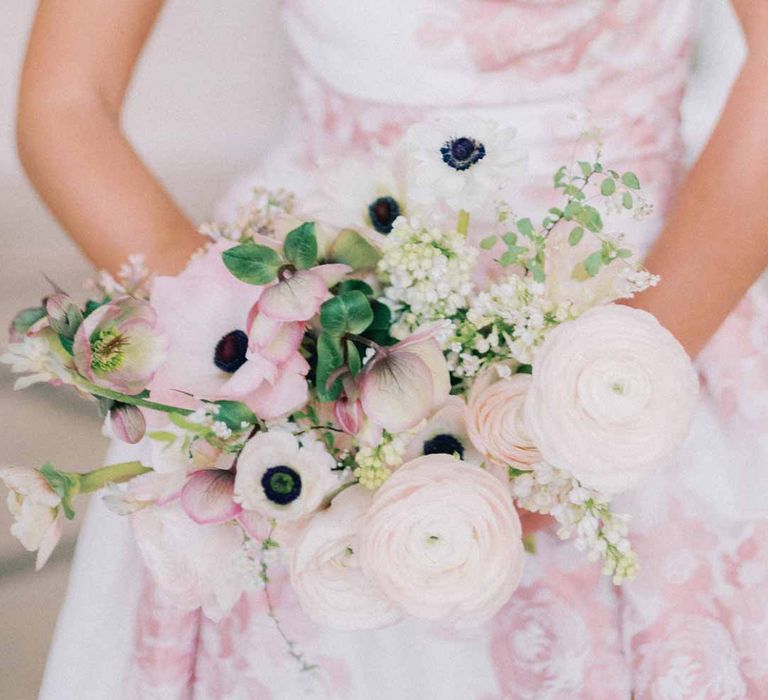 Bride wearing off the shoulder white and pink floral patterned bridal gown with black bow and front slit holding bridal bouquet with white poppies, light pink Persian buttercups, baby's-breath and foliage 