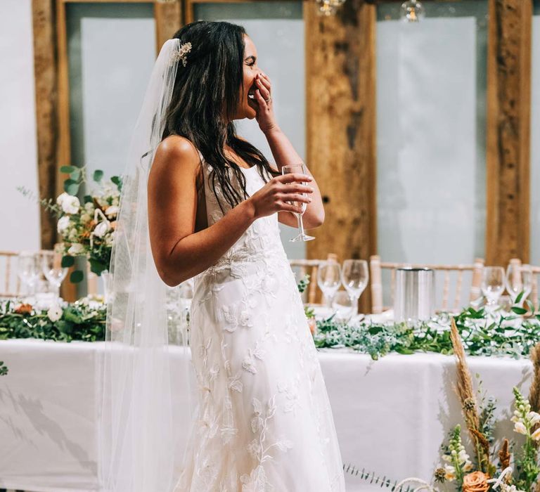 Bride in a-line tulle wedding dress with beaded lace applique with petals and a square neckline with side tulle cutouts and church length veil standing in reception room during wedding breakfast at South Farm wedding