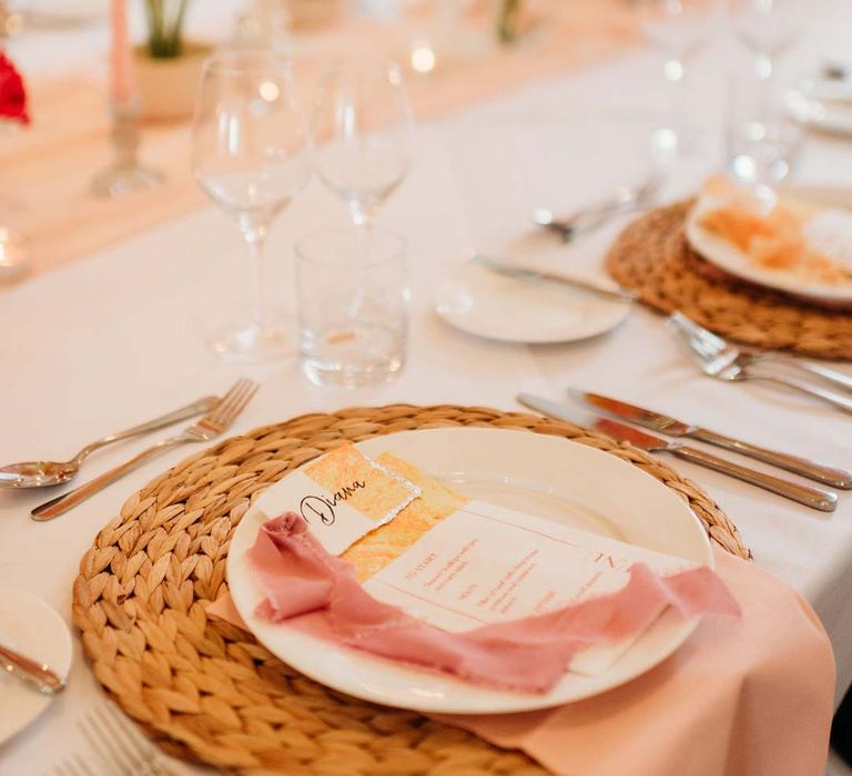 Wedding tablescape with white wedding tablecloth, burlap place mats, tapered candles, pink and orange wedding stationery, and floral wedding table centrepieces