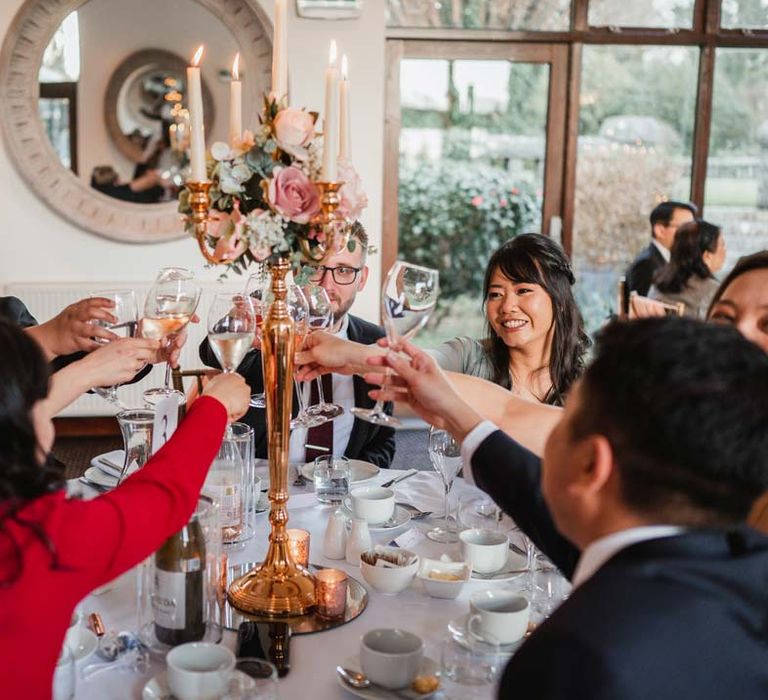 Wedding guests cheering their drinks with rose gold candelabra in the middle at Burmese wedding