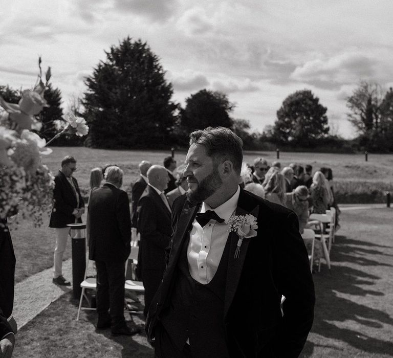 Groom in black tuxedo at outdoor wedding waiting for the bride 