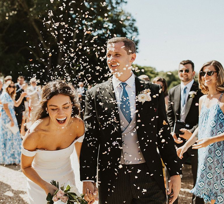 Bride and groom exit from their classic wedding ceremony to their guests throwing confetti in celebration