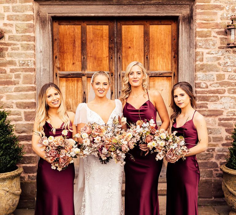 Satin burgundy cowl neck bridesmaid dresses with bride in lace wedding dress at country house wedding venue