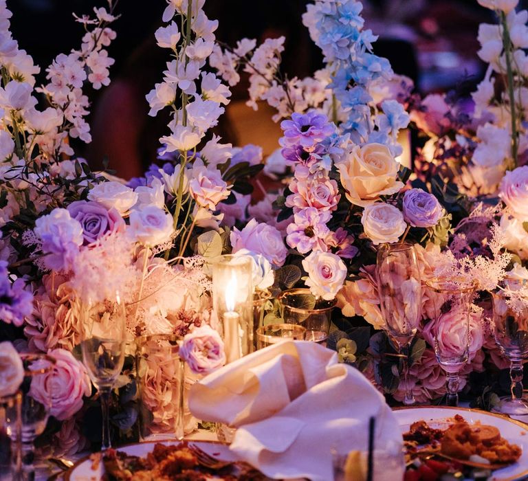 Botanical wedding tablescape at Syon Park vow renewal with large pastel flower centrepieces, gold tapered candles, gold rimmed tableware and suspended pastel foliage decor 