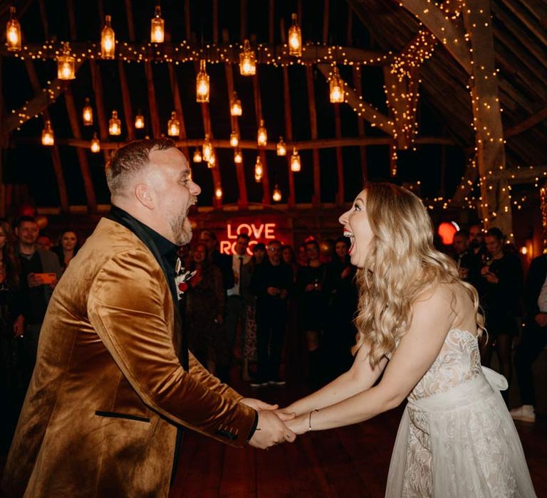 Groom in crushed velvet burnt orange grooms blazer and dried flower boutonniere dancing with bride in off shoulder lace wedding dress with corset style top at Southlands Barn wedding venue